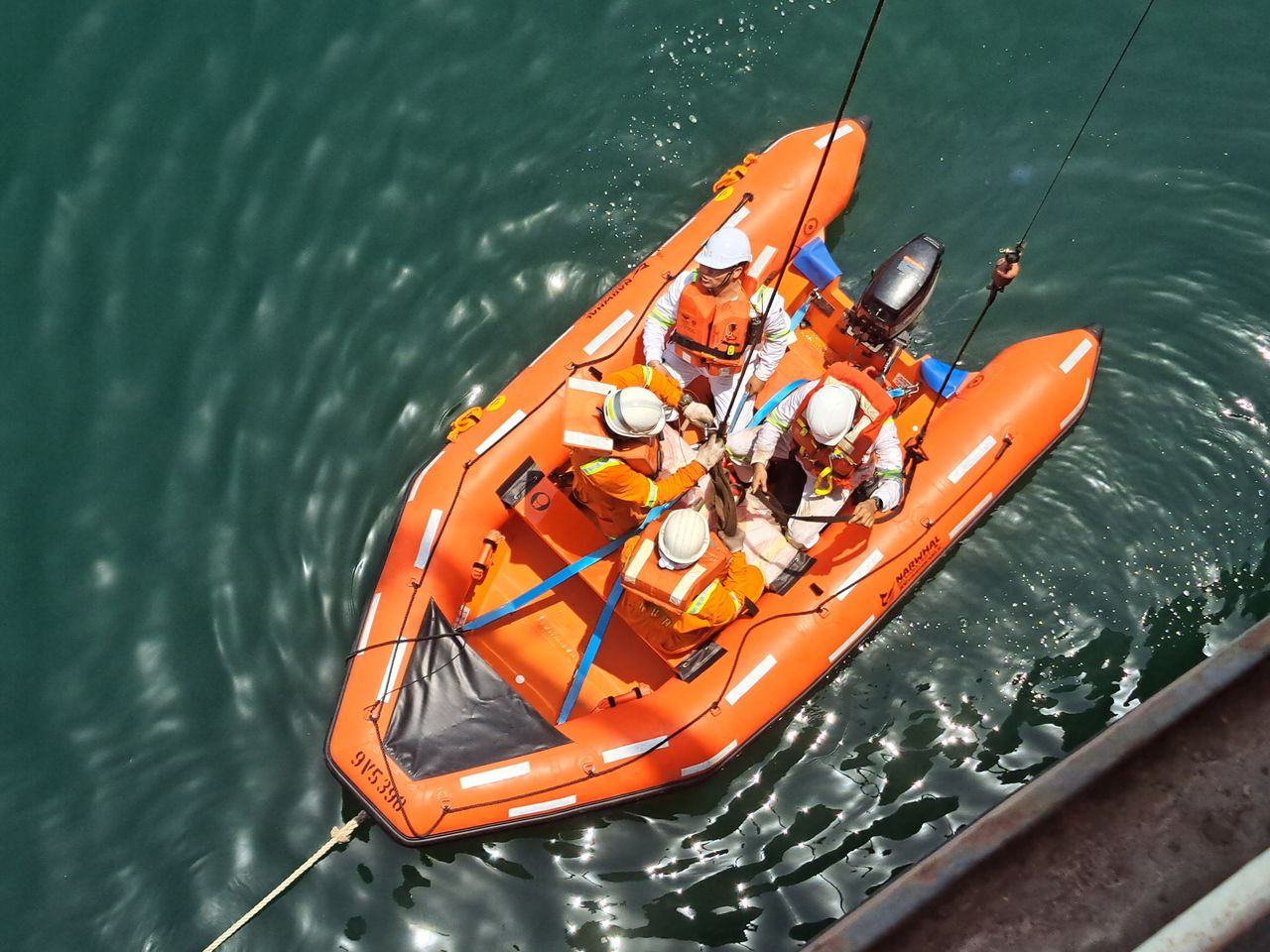 Aerial view of rescue personnel conducting a safety drill on an orange boat in the ocean.
