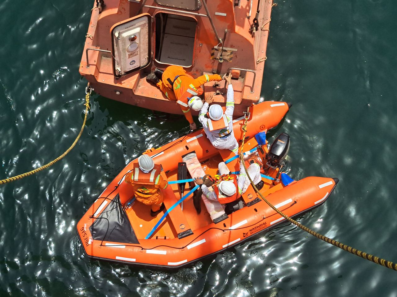 A team conducts a rescue operation on a lifeboat at sea. Captured from above.