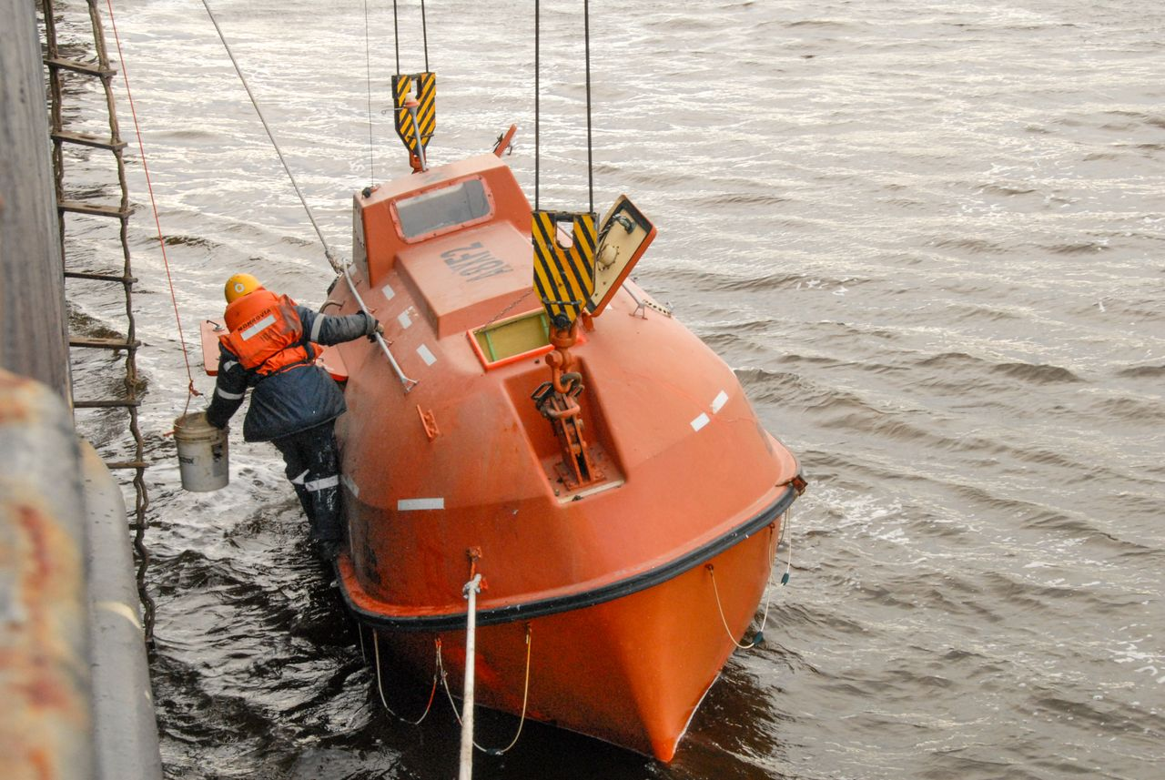 A safety drill featuring a person boarding an orange lifeboat at sea.
