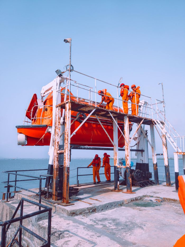 Crew in orange uniforms preparing lifeboat for marine safety operations at Indian coastal station.